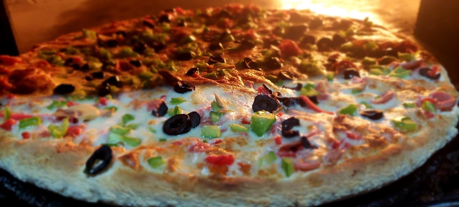 A pizza baking on the stone floor of the wood fired oven at Pizza Time, flames along the back wall.